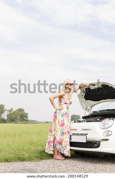 Full-length of tensed woman standing by broken down\
car on country road
