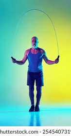 Full-length vertical image of elderly man in sportswear training, jumping rope against gradient green yellow background in neon light. Concept of sport, active elderly lifestyle, health care