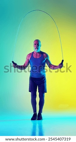 Full-length vertical image of elderly man in sportswear training, jumping rope against gradient green yellow background in neon light. Concept of sport, active elderly lifestyle, health care