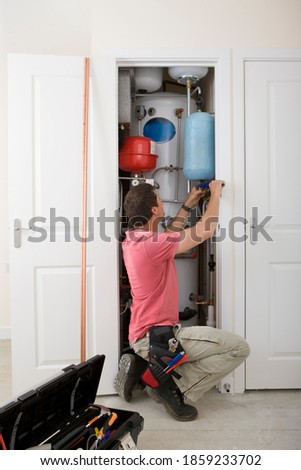 A full-length vertical view of a middle-aged handyman fixing boiler in the closet