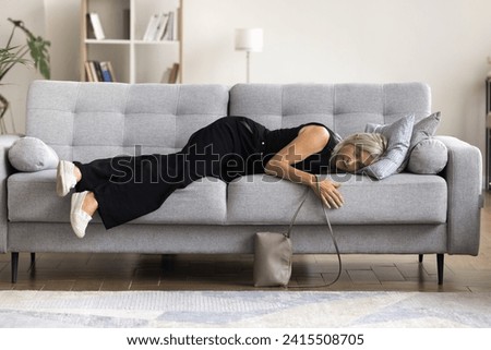 Full-length view tired mature woman felt asleep on sofa, arrive at home after party or hard-working day, flopped down on couch looks squeezed like lemon, need rest for restoring. Overwork, exhaustion