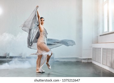 Full-size Expressive Photo Of Female Ballet Dancer Dressed In Grey-blue Flowing Fabric Spinning On One Leg On White Y Background.