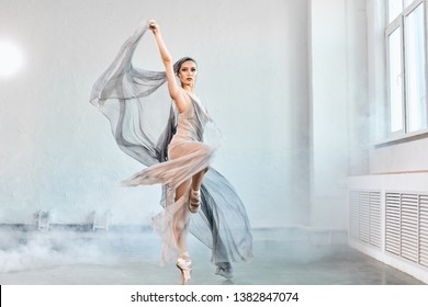 Full-size Expressive Photo Of Female Ballet Dancer Dressed In Grey-blue Flowing Fabric Spinning On One Leg On White Y Background.