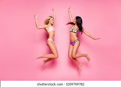 Full-size full-length photo of beautiful attractive cute lovely cheerful joyful women clothes in bikini, they are jumping up and giving high five in the air, isolated on bright pink background
