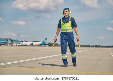 Full-sized portrait of a serious aircraft marshaller with wands walking alone across the airfield