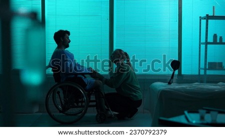 Full-sized silhouette shot of a disabled man, patient with mobility impairment on a wheelchair, talking happily to a young woman, his girfriend, wife or relative.