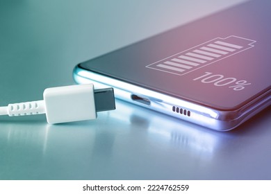 Fully charged battery icon on the touch screen of the cell phone and a USB Type-C cable. Fully charged smartphone battery. Keeping the battery intact. Battery safety. Copy space