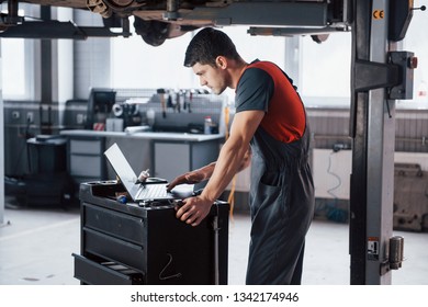 Fully concentrated. Man at the workshop in uniform using laptop for his job for fixing broken car. - Powered by Shutterstock