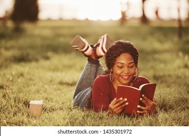 Fully concentrating on reading interesting book. Cheerful african american woman in the park at summertime.