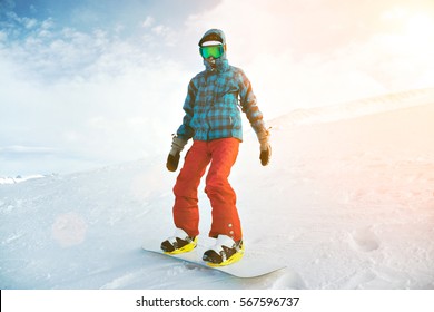 Fully equipped and covered from cold beginner girl snowboarder wears her google mask, stands alone at top of ski slope on backside edge, near ski lift in sun rays, ready to ride down