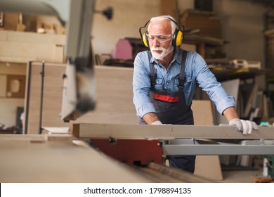 Fully equipped smiling senior carpenter operating on a woodworking machine - Powered by Shutterstock