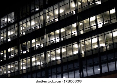 Fully Lit Office Building At Night With  Cubicles Visible Through Windows