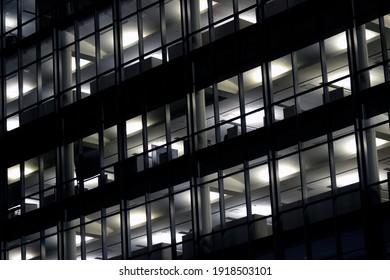 Fully Lit Office Building At Night With  Cubicles Visible Through Windows