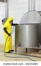 Fully protected specialist in uniform,mask,gloves,boots and with hose at industrial process tank