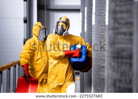 Fully protected workers in yellow hazmat suit, gas masks and gloves handling dangerous chemicals or substances.