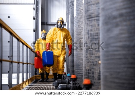Fully protected workers in yellow suit, gas masks and gloves handling dangerous chemicals or substances.