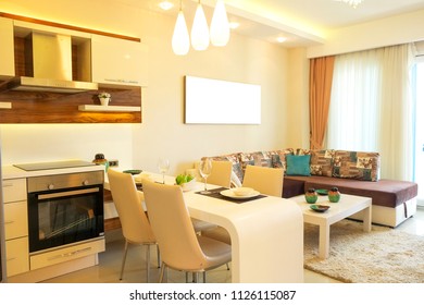 Fully stacked open plan kitchen living room in minimal modern design interior apartment w/ full length windows. Counter w/ tableware, table settings, oven, sofa, shelves, decor elements. Background.