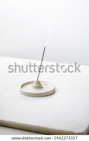 Fuming incense stick in porcelain craft ceramic holder on white marble table with white background.