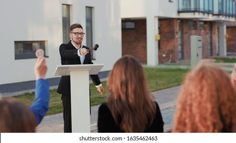 Fun auction sale. Back view of rich bidders raising hands bidding for real estate objetcs sitting outdoors. Charismatic male auctioneer leading a property auction. - Shutterstock ID 1635462463