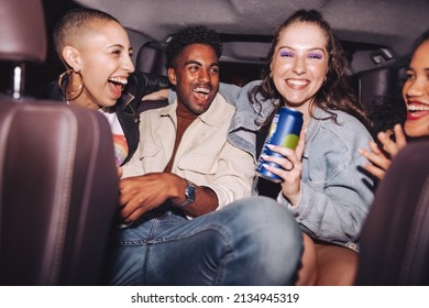 Fun In The Back Seat. Group Of Four Happy Friends Laughing Together While Sitting Together In The Back Of A Car. Carefree Friends Having A Good Time In Their Ride Home After A Party.