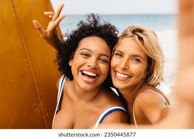 Fun beach memories are made as female surfers flash bright smiles for a selfie, encapsulating the carefree spirit and the thrilling experiences of their unforgettable surfing trip. - Powered by Shutterstock