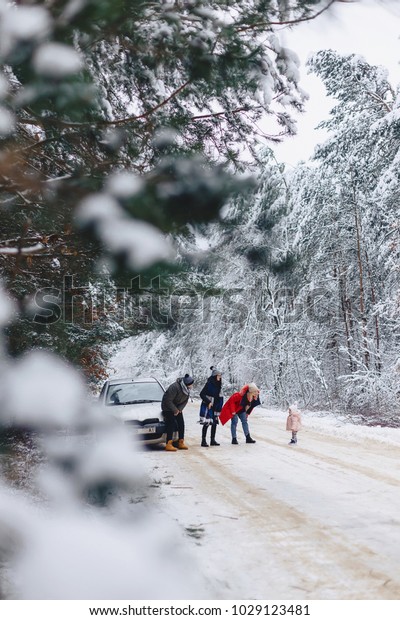 fun company with a little\
baby on a snowy road under winter pine trees stopped and walk\
around the car