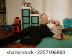 A fun dad is lying down on the floor with his only child, hugging him, and playing fun games. Family love, healthy development. A cheerful infant is laughing while his father is playing with him.