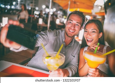 Fun date night out young people taking selfie of themselves drinking giant margaritas cocktails party couple going out on Miami Ocean drive restaurant. Funny drinks outdoor terrace travel lifestyle. - Powered by Shutterstock