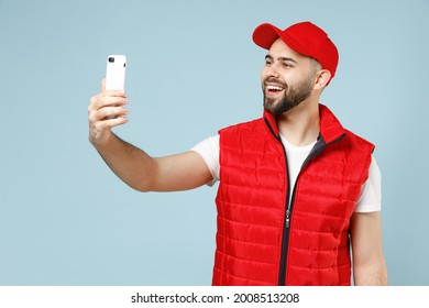 Fun Delivery Guy Employee Man In Red Cap White T-shirt Vest Uniform Workwear Work As Dealer Courier Hold Use Mobile Cell Phone Isolated On Pastel Blue Color Background Studio Portrait. Service Concept