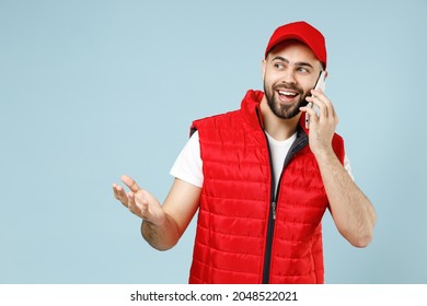 Fun Delivery Guy Employee Man In Red Cap White T-shirt Vest Uniform Workwear Work As Dealer Courier Hold Use Mobile Cell Phone Isolated On Pastel Blue Color Background Studio Portrait. Service Concept