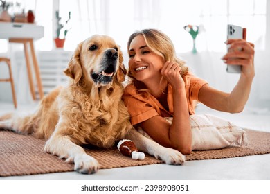 Fun with domestic animal. Loving pet owner taking selfie on smartphone while lying on floor near golden retriever. Cheerful female cuddling on best dog companion and enjoying daily interaction. - Powered by Shutterstock