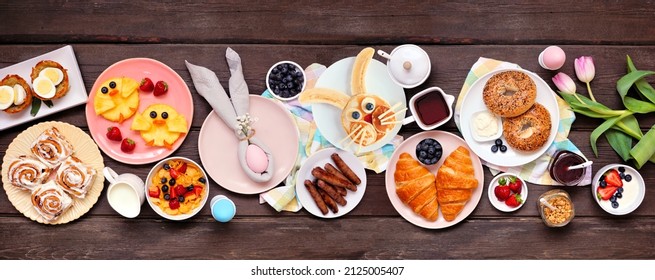 Fun Easter Breakfast Or Brunch Table Scene. Above View On A Dark Wood Banner Background. Bunny Pancake, Egg Nests, Chick Fruit And A Selection Of Spring Food Items.