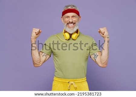 Fun elderly gray-haired bearded man 40s years old in headband khaki t-shirt showing biceps muscles on hand demonstrating strength power isolated on plain pastel light purple background studio portrait