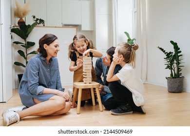 Fun family playing jenga on the floor, pulling tiles out of tower on a stool. Parents and children sitting in a circle. - Shutterstock ID 2144509469