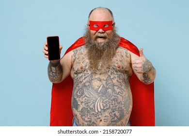 Fun Fat Pudge Obese Chubby Overweight Blue-eyed Bearded Man 30s In Red Cartoon Character Cloak Mask Naked Torso Hold Mobile Cell Phone With Blank Screen Area Show Thumb Up Isolated On Blue Background