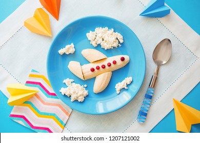 Fun Food Idea For Kids. Children's Breakfast: Plane Made Of Banana And Clouds Made Of Curd On A Blue Plate. Dreams Of Flying. Creative Lunch Of The Future Pilot.