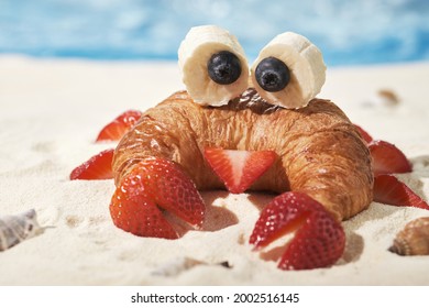 Fun Food for kids. Cute crab croissant with fruit for kids breakfast on the sea sand beach