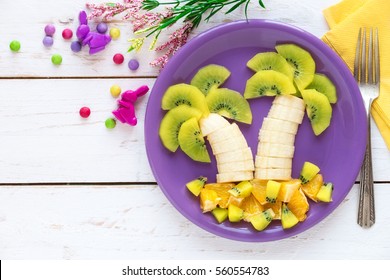 Fun Food For Kids - Fruit Palms Made Of Fresh Bananas, Kiwi And Orange Slices On Purple Plate Against White Wooden Table With Easter Decorations