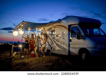 Fun with friends in camp, in front of rv. Young group of people dancing, playing guitar, and celebrating. Summertime togetherness. Travel, weekend, lifestyle concept.
