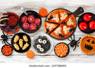 Fun Halloween Dinner Party Table Scene Over A White Wood Background. Overhead View. Ghost Pizza, Eyeball Spaghetti, Jack O Lantern Pumpkin Pie, Candy Apples, Snacks And Spooky Punch.