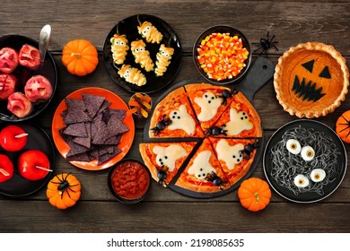 Fun Halloween dinner party table scene over a dark wood background. Top view. Pizza, jack o lantern pumpkin pie, candy apples, eyeball spaghetti, snacks and spooky punch. - Shutterstock ID 2198085635
