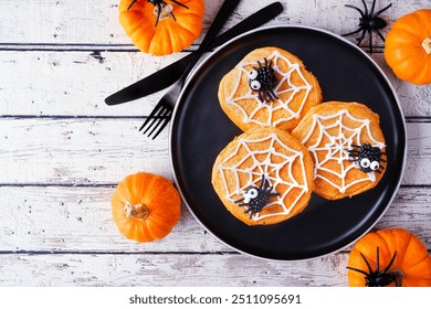 Fun Halloween spider web pumpkin pancakes with blackberry spiders. Overhead view on a black plate against a rustic white wood table background. - Powered by Shutterstock