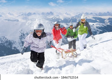 A Fun And Happy Family Running Together In The Snow While Pulling A Sled Uphill On A Steep Slope