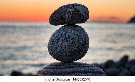 Fun holiday at sea, beach activities. The pyramid (cone) is built of round stones (small boulders) in balance (equilibrium), against sunset. Variegated and striped stones of different shapes