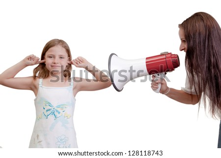 Fun humorous image of a naughty little girl playing deaf sticking her fingers in her ears while her mother shouts at her with a megaphone isolated on white