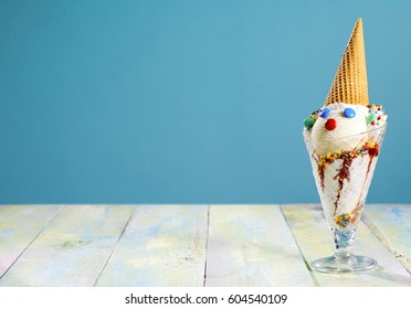 Fun Ice Cream Sundae For A Kids Party With A Cute Little Clowns Face Decorated With Sugar Coated Candy And A Cone For A Hat On A Rustic Table With Copy Space Over Blue