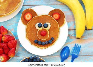 Fun idea for kids breakfast. Bear shaped pancakes with berries on blue wooden table, top view. Healthy food for children. Funny food for kids