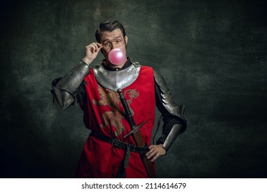 Fun, joy. Comic portrait of funny medieval warrior or knight with dirty wounded face holding sword isolated over dark background. Comparison of eras, history, renaissance style. Art, meme