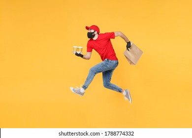 Fun Jumping Delivery Man Guy Employee In Red Cap Mask Gloves Hold Craft Paper Packet Food Coffee Isolated On Yellow Background Studio. Service Quarantine Pandemic Coronavirus Virus 2019-ncov Concept