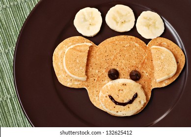 Fun kid's breakfast of a smiling monkey face with chocolate chips for eyes on plate with banana slices. - Powered by Shutterstock